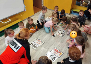 Grupa dzieci przygląda się numerom alarmowym pokazanym na planszy