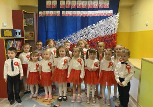 Reprezentacja przedszkola w galowych strojach z kotylionami na piersi śpiewa Hymn