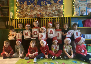 Dzieci z grupy I w świątecznych czapeczkach trzymające napis Mikołajki