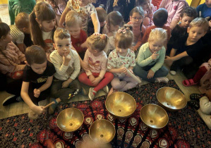Oliwier uderza pałeczką w misę i dzieci wsłuchują się w wybrzmiewające dźwięki