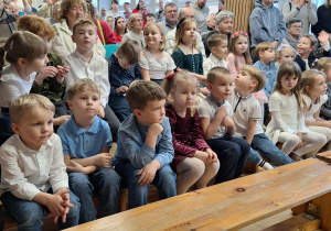 Dzieci z Przedszkola Miejskiego nr 164 siedzą na ławeczkach i niecierpliwie czekają na występy.