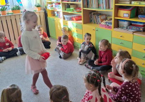 dziewczynka chodzi po kole z pluszowym serduszkiem a wokół niej siedzą dzieci w sali na dywanie