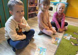 Otylia, Kinga i Kacper układają obrazki z dinozaurami