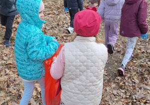 Dziewczynki niosą worek ze śmieciami a przed nimi grupka dzieci idzie przed siebie